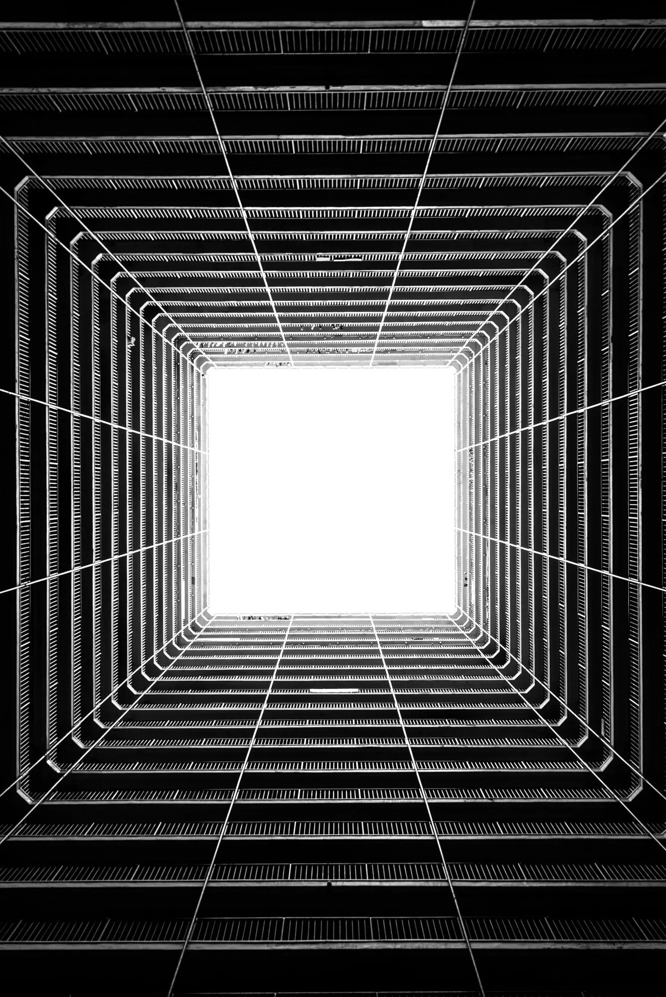 A vertical greyscale low-angle shot showing light coming through the ceiling of a tall building.