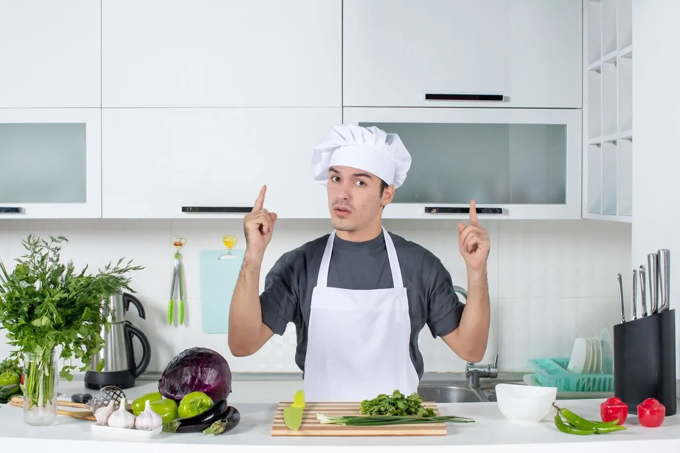Front-facing view of a young chef in uniform pointing at the ceiling.